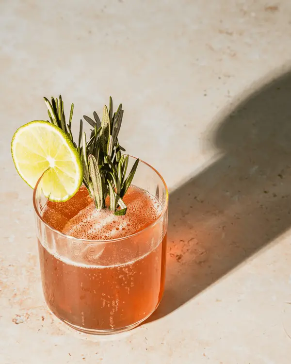 A craft drink in a tall glass garnished with lime and rosemary