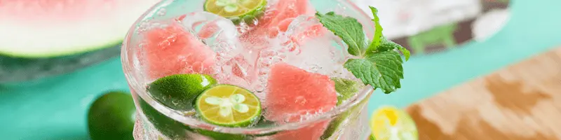 A glass of watermelon and lime infused water with mint on a wooden board